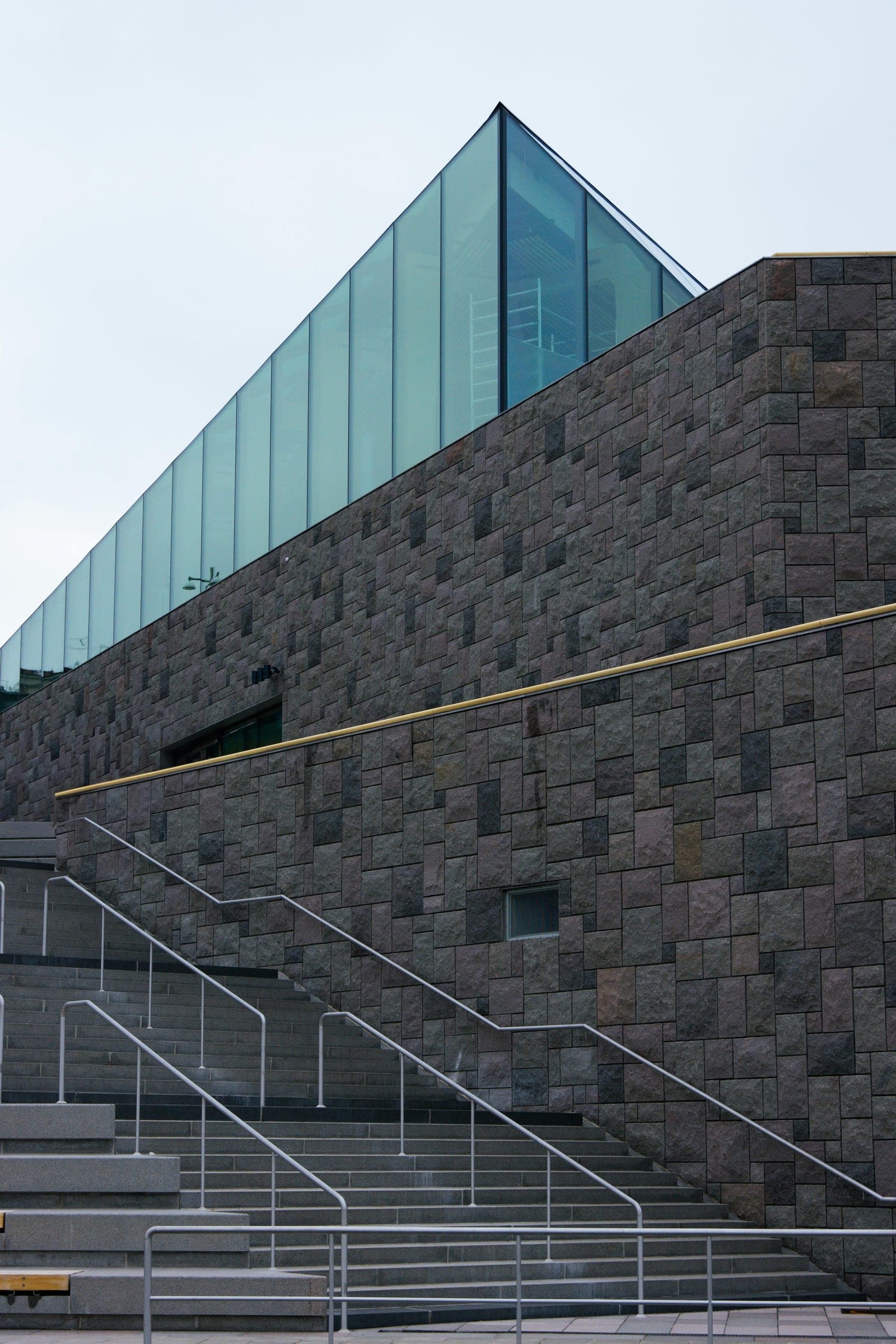 Lågvinkel mot en modern glasfasad som speglar blå himmel och moln; diagonalt snitt mot himlen.